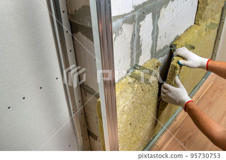 Worker insulating a room wall with mineral rock wool thermal insulation. 95730753