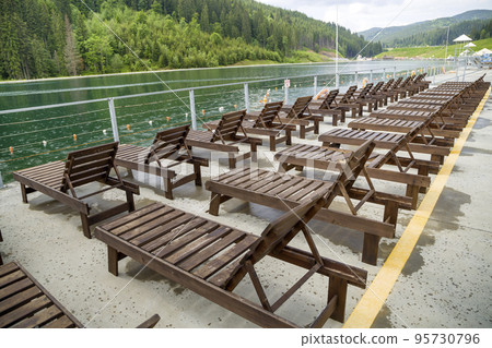Row of empty wooden beach chairs near water. Row of empty wooden beach chairs near water. 95730796