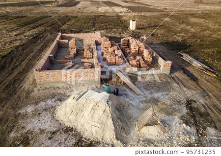 Aerial view of building site. Trenches dug in ground and filled with cement as foundation for future house, brick basement floor and stacks of brick for construction. Aerial view of building site. Trenches dug in ground and filled with cement as foundation for future house, brick basement floor and stacks of brick for construction. 95731235
