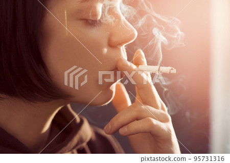 Girl is holding a cigarette in her hand, smoking closeup Girl is holding a cigarette in her hand, smoking closeup 95731316