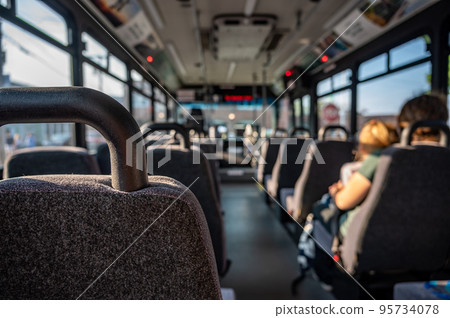 Focus on an empty seat in a bus with only a single mother and child in the distance. Focus on an empty seat in a bus with only a single mother and child in the distance. 95734078