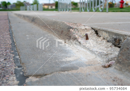 Broken sidewalk curb with exposed rebar and jagged edges that could cause a tripping hazard 95734084