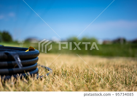 Coil of 1 inch irrigation tubing ready for new installation on top of brown and damaged dry grass. 95734085