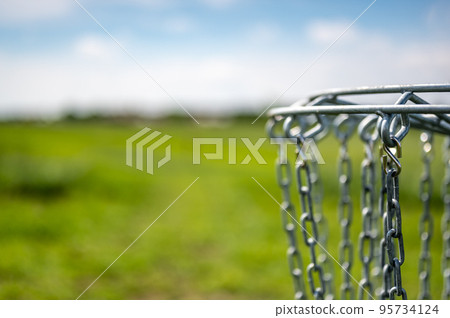 Disc golf goal chains gently swaying in the breeze with a green course in the background Disc golf goal chains gently swaying in the breeze with a green course in the background 95734124
