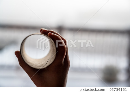Child holding a cardboard toilet paper tube as a telescope to see through to imagine another world 95734161