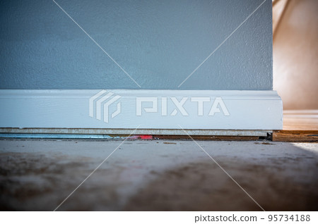 Bare plywood ready for carpet installation against a wall with white baseboard and a hardwood transition.  95734188
