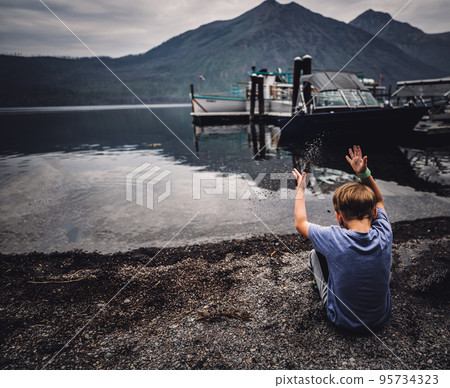 Young boy tossing sand into Lake McDonald at Glacier National Park 95734323