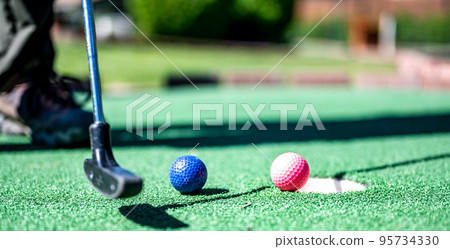 Mini golf game with several colored balls in the way of a putter lined up. Mini golf game with several colored balls in the way of a putter lined up. 95734330