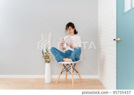 Asian woman sitting on a chair and reading at home (reading a book) Asian woman sitting on a chair and reading at home (reading a book) 95735437