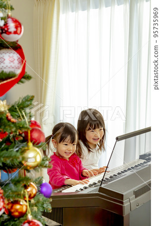 Sisters playing the electone next to the Christmas tree 95735969