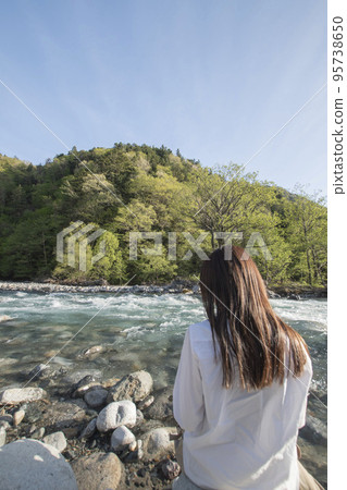 A woman enjoying nature on a river in sunny Kamikochi 95738650