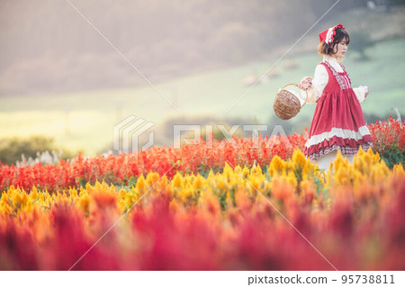 A woman dressed as Little Red Riding Hood looking happy in the flower garden A woman dressed as Little Red Riding Hood looking happy in the flower garden 95738811