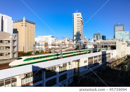 Tohoku Shinkansen E2 series 200 series painted formation with buildings in the background Tohoku Shinkansen E2 series 200 series painted formation with buildings in the background 95739094