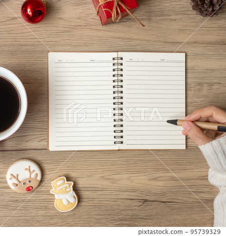 Woman hand writing on notebook with black coffee cup and Christmas cookies on table. Xmas, Happy New Year, Goals, Resolution, To do list, Strategy and Plan concept 95739329