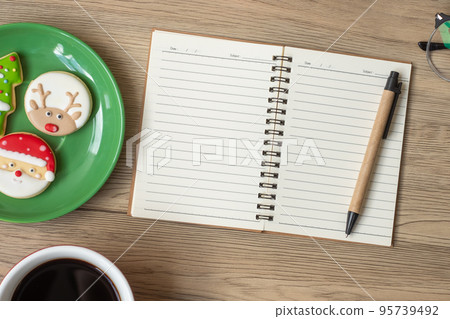 Blank notebook, black coffee cup, Christmas cookies and pen on wood table, Top view and copy space. Xmas, Happy New Year, Goals, Resolution, To do list, Strategy and Plan concept 95739492