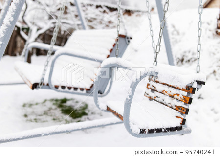 Snow covered wooden white swing after heavy snow. Winter frosty day 95740241