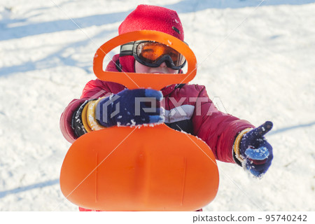 A boy is riding a sledge in snowy park in winter. Child outdoor activities 95740242