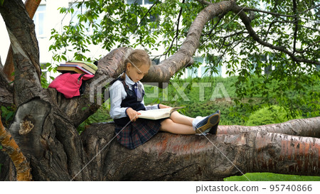 Schoolgirl relaxing on a tree branch while reading a book. Literature, education and back to school concept Schoolgirl relaxing on a tree branch while reading a book. Literature, education and back to school concept 95740866