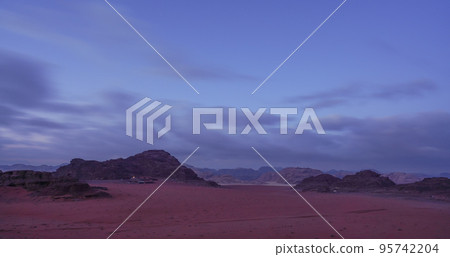 Rocky scenery in Wadi Rum desert during early overcast morning, camp light at distance visible 95742204