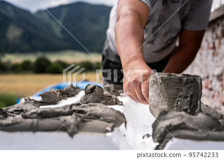 Installing white polystyrene heat insulation, detail on worker hand putting gray bonding cement glue on white boards 95742233