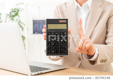 A middle-aged woman wearing a suit holding a calculator and raising her index finger 95744146