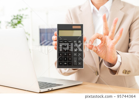 Middle woman wearing a suit holding a calculator and making a circle sign Middle woman wearing a suit holding a calculator and making a circle sign 95744364