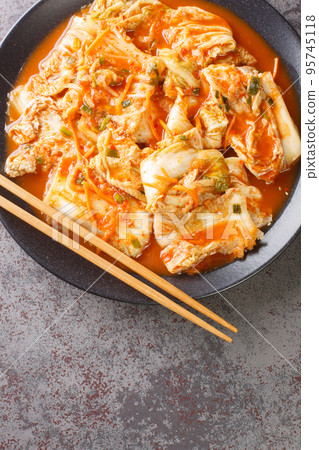 Korean Food Traditional Kimchi napa cabbage with carrot, daicon, onion, garlic and spice closeup in a black dish. Vertical top view Korean Food Traditional Kimchi napa cabbage with carrot, daicon, onion, garlic and spice closeup in a black dish. Vertical top view 95745118