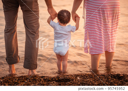 Father and mother hold hands of a small child and go to sea. Beach and ocean at background. Back view. The concept of fostering family happiness 95745952