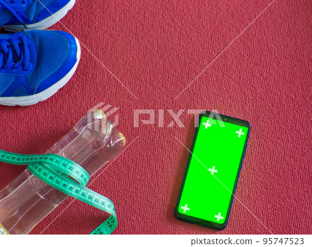 Sneakers, laptop, water bottle and measuring tape on a red yoga mat 95747523