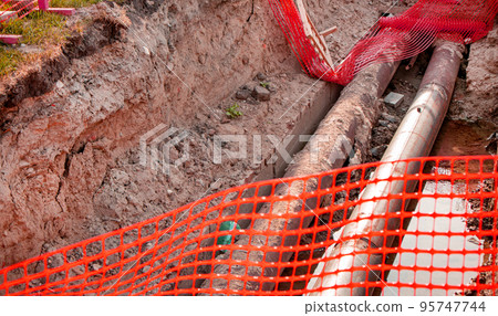 Repair of the heating plant system with the laying of new underground metal pipes in the trench. Reconstruction of the city heating system. Mesh fencing for work safety Repair of the heating plant system with the laying of new underground metal pipes in the trench. Reconstruction of the city heating system. Mesh fencing for work safety 95747744