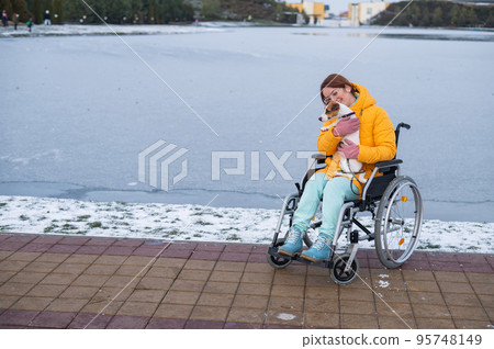 Caucasian woman in a wheelchair walks the dog in winter. Caucasian woman in a wheelchair walks the dog in winter. 95748149