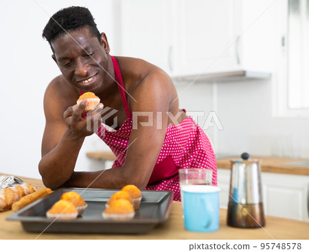 Portrait of handsome man in apron with hot cupcakes at home Portrait of handsome man in apron with hot cupcakes at home 95748578
