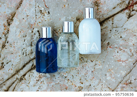 Three plastic or glass cosmetic bottles, containers with shampoo, shower gel, body lotion for facial skin care - on natural beige stone rock background top view. Natural eco-friendly cosmetics. 95750636