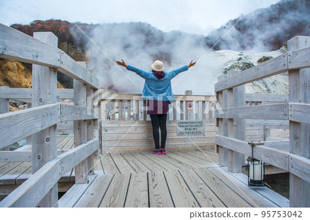 Woman standing at Jigokudani or Hell Valley in the town of Noboribetsu Onsen, hot steam vents, sulfurous streams and other volcanic activity, hot spring waters, Hokkaido, Japan, traveling concept. Woman standing at Jigokudani or Hell Valley in the town of Noboribetsu Onsen, hot steam vents, sulfurous streams and other volcanic activity, hot spring waters, Hokkaido, Japan, traveling concept. 95753042