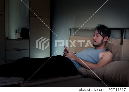 Asian Young man using Mobile Phone on the bed at night.. Asian Young man using Mobile Phone on the bed at night.. 95753217
