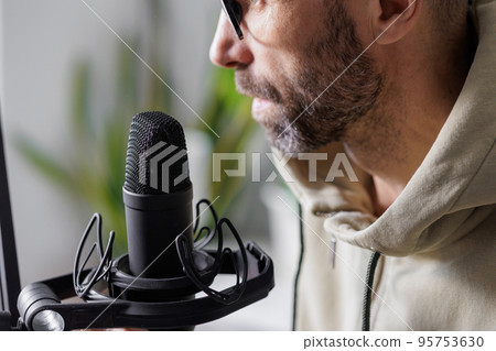 man records a podcast or audio content in a home office. a successful adult man with headphones man records a podcast or audio content in a home office. a successful adult man with headphones 95753630
