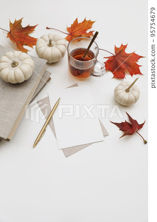 Fall still life. Autumn stationery. Blank greeting card, invitation mockup. Pumpkins, red maple leaves isolated on white table background. Breakfast scene. Glass cup of tea, golden pen and book. Top 95754679