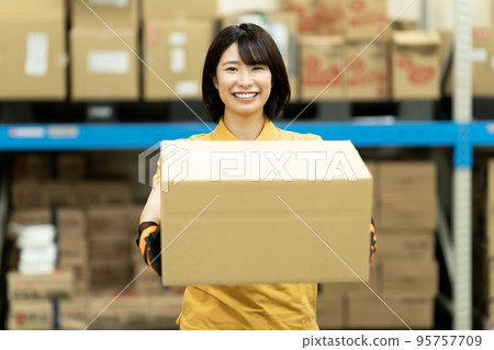 Female staff carrying cardboard boxes in warehouse 95757709