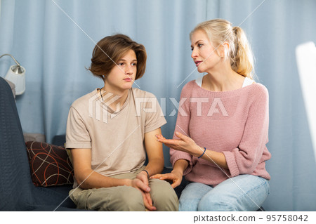 Troubled teen boy sitting at home while his mother scolding him 95758042