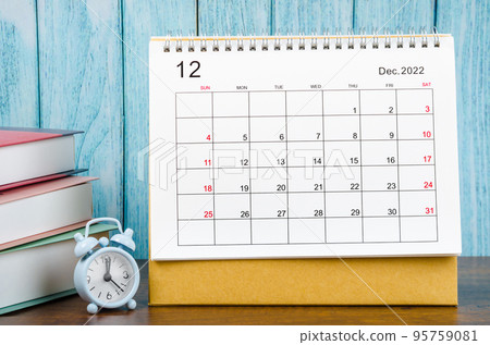 The December 2022 Monthly desk calendar for the organizer to plan 2022 year with alarm clock and books on wooden table. 95759081