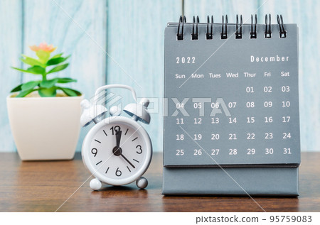 The December 2022 Monthly desk calendar for 2022 year with alarm clock on blue wooden background. 95759083