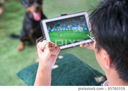 Watching soccer game on digital tablet. 95760359