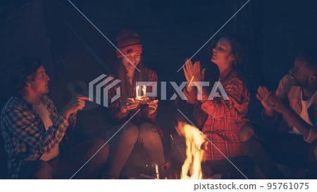 Attractive young woman hiker is celebrating birthday in forest getting cake blowing candles while her friends are clapping hands and shouting. Celebration, fun and nature concept. Attractive young woman hiker is celebrating birthday in forest getting cake blowing candles while her friends are clapping hands and shouting. Celebration, fun and nature concept. 95761075