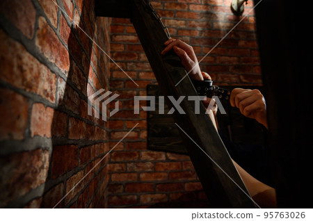 BDSM Close-up of hands in handcuffs. The man dominates and rivets his mistress to the Andreev cross. Games for adults. Brick wall. Red room. BDSM Close-up of hands in handcuffs. The man dominates and rivets his mistress to the Andreev cross. Games for adults. Brick wall. Red room. 95763026