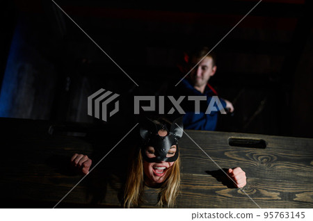nipple tapes. A woman is imprisoned in a wooden pillory during sexual games. BDSM Erotic fantasies. Subordination. Toys for adults. The mask of the cat. The man in the shirt dominates. 95763145