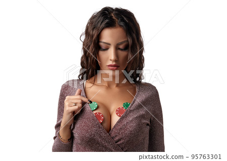 Brunette woman wearing in shiny brown dress. There are some green and red chips on her breast. Isolated on white background. Casino, poker. Close-up. 95763301