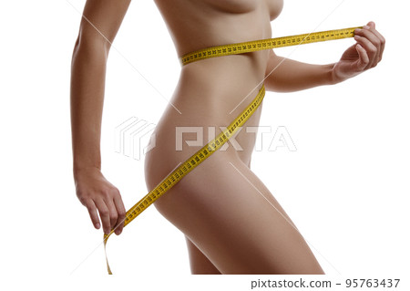 Perfect body of a nude girl measuring herself while posing isolated on white. Plastic surgery and aesthetic cosmetology concept. Close-up. Perfect body of a nude girl measuring herself while posing isolated on white. Plastic surgery and aesthetic cosmetology concept. Close-up. 95763437