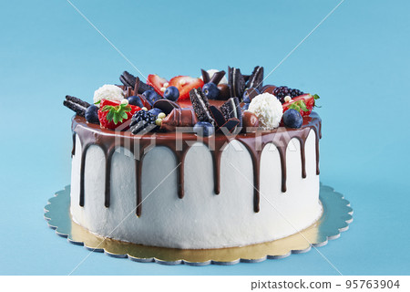 Birthday cake on blue background. Close up of cake decorated with fresh berries and chocolate sweets on color background. Delicious dessert for party Birthday cake on blue background. Close up of cake decorated with fresh berries and chocolate sweets on color background. Delicious dessert for party 95763904