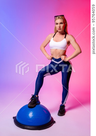 Fit woman in sportswear standing in neon light studio 95764059