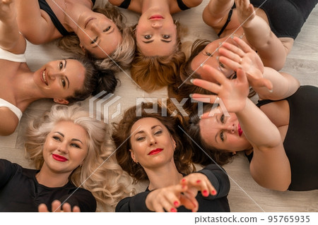 Seven happy women lie on their backs on the floor with their heads pressed together. Seven happy women lie on their backs on the floor with their heads pressed together. 95765935